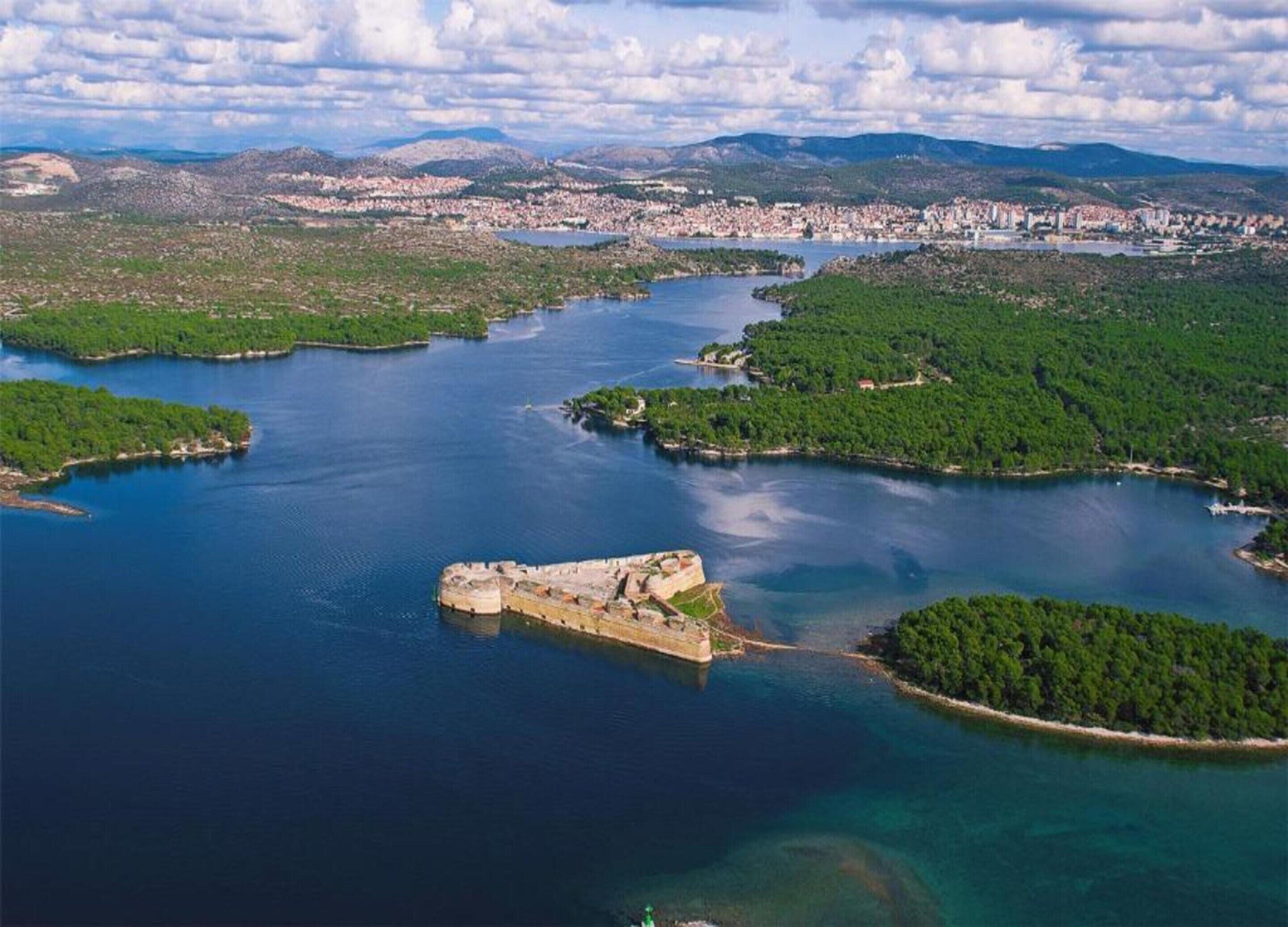 Vue aérienne d’une zone côtière avec une structure fortifiée entourée d’eau et de végétation.