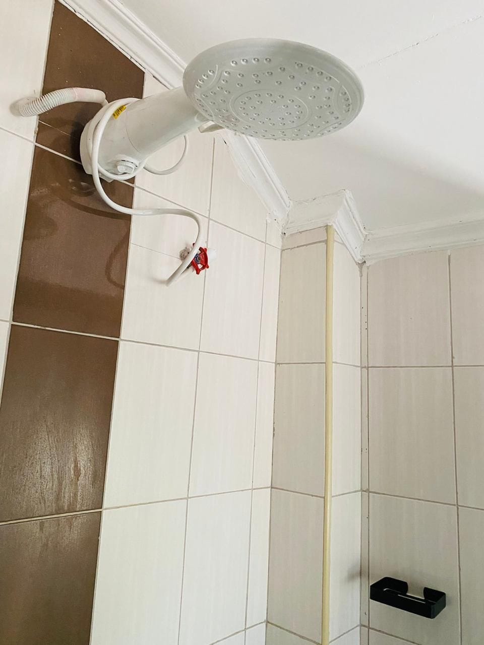 Eine Dusche mit Handbrause, einer weißen Wand und braunen Bodenfliesen.