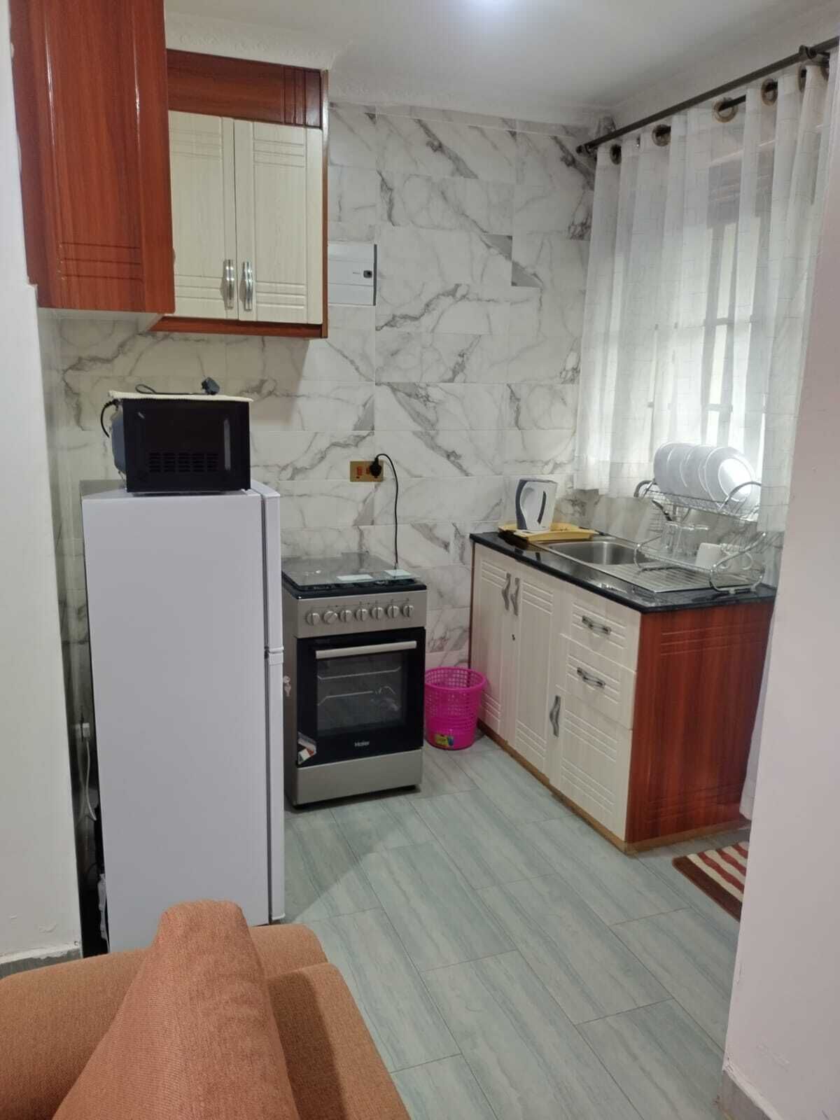 Eine kleine Küche mit Kühlschrank, Backofen, Mikrowelle und Spüle mit Geschirrgestell.