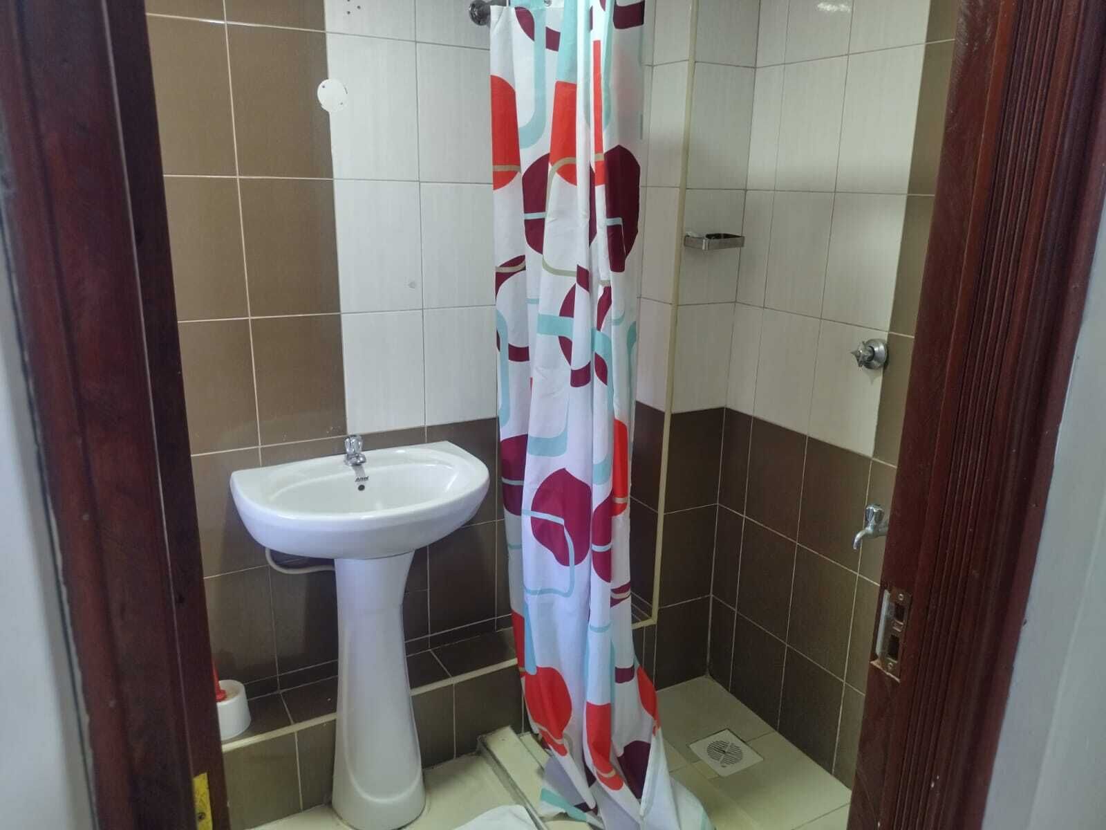 Un bagno con un lavandino su piedistallo, una tenda da doccia e pareti piastrellate.