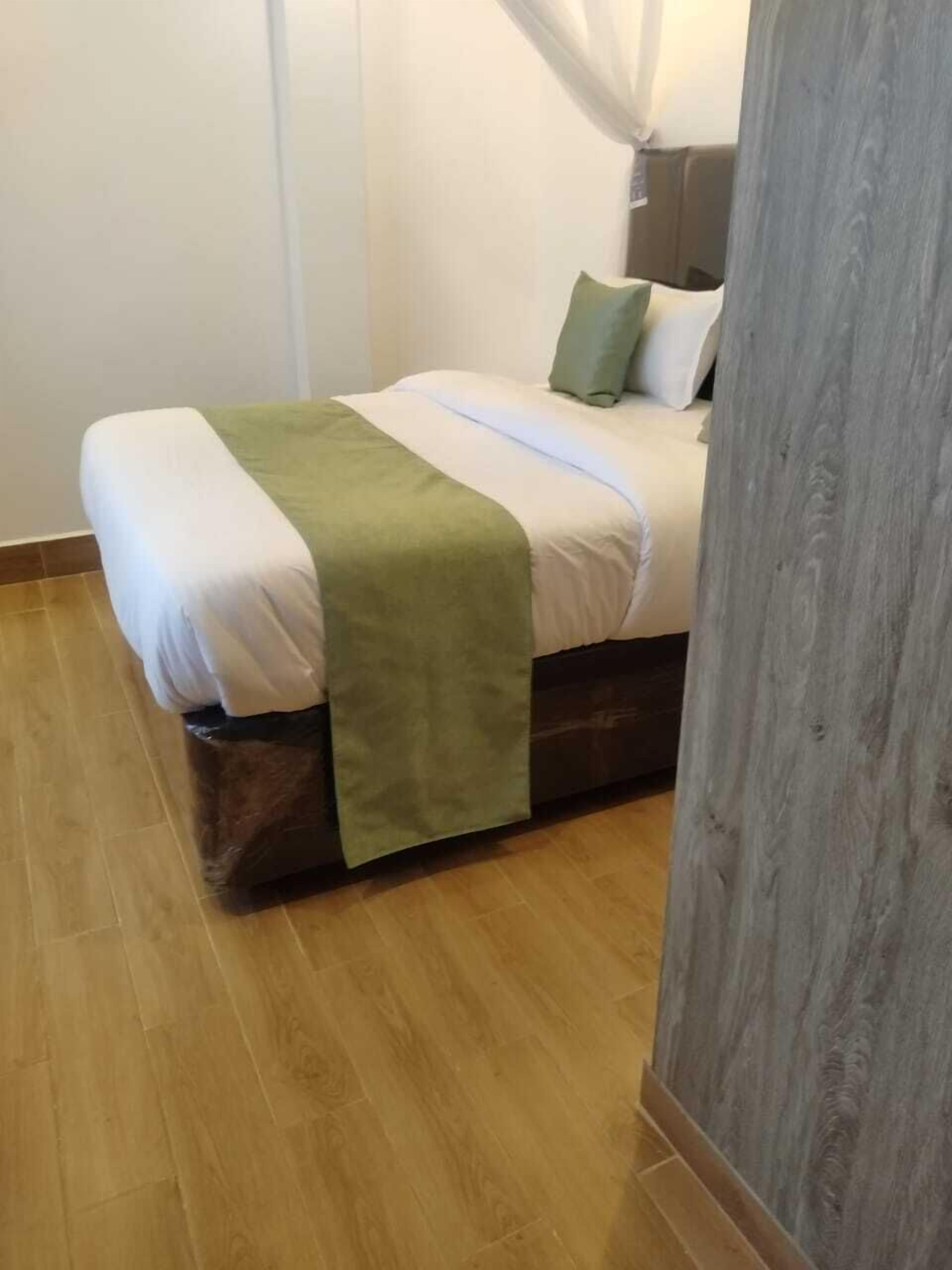 Ein ordentlich bezogenes Bett mit einer grünen Tagesdecke, einem hölzernen Kopfteil und einem Holzboden.