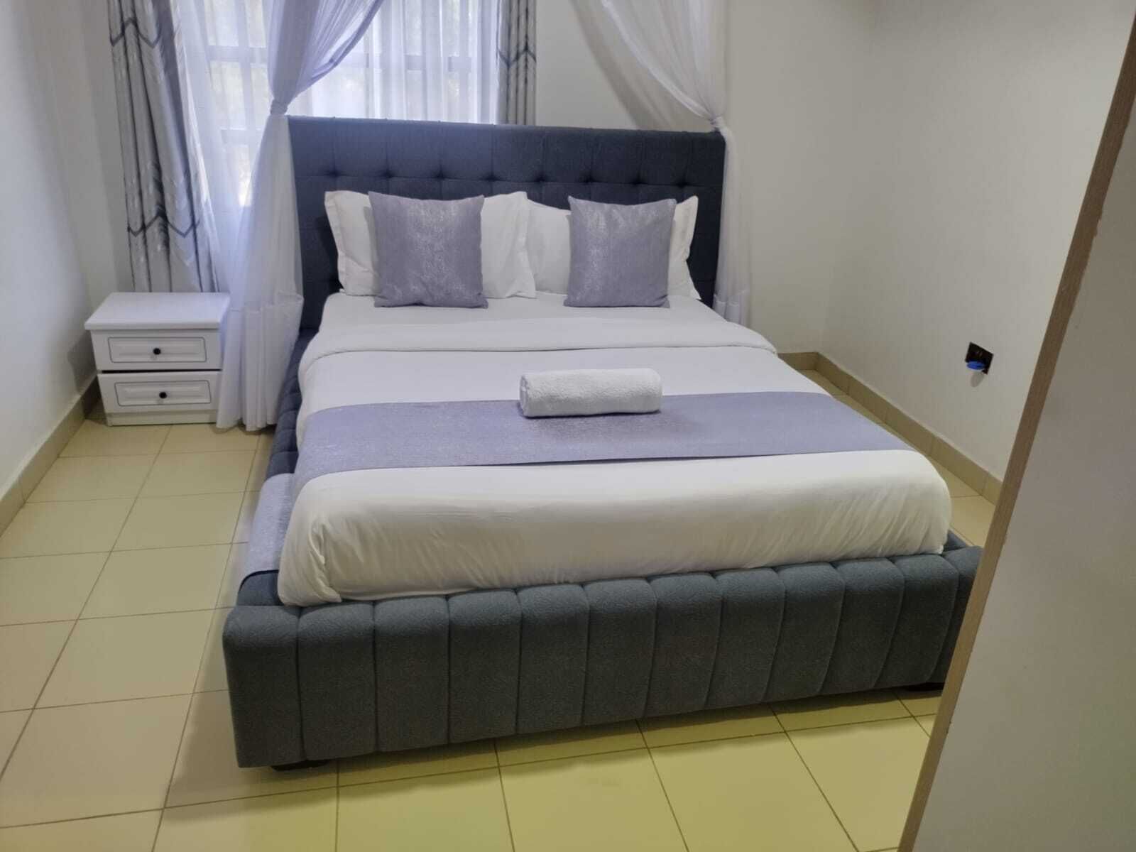 Una cama bien hecha con un cabecero tapizado en gris, ropa de cama blanca y una manta gris.
