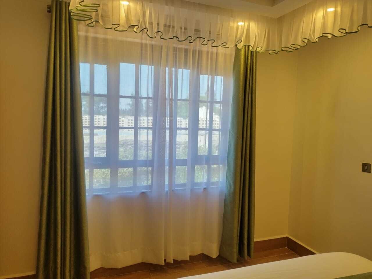 A room with a large window, curtains, and a bed.