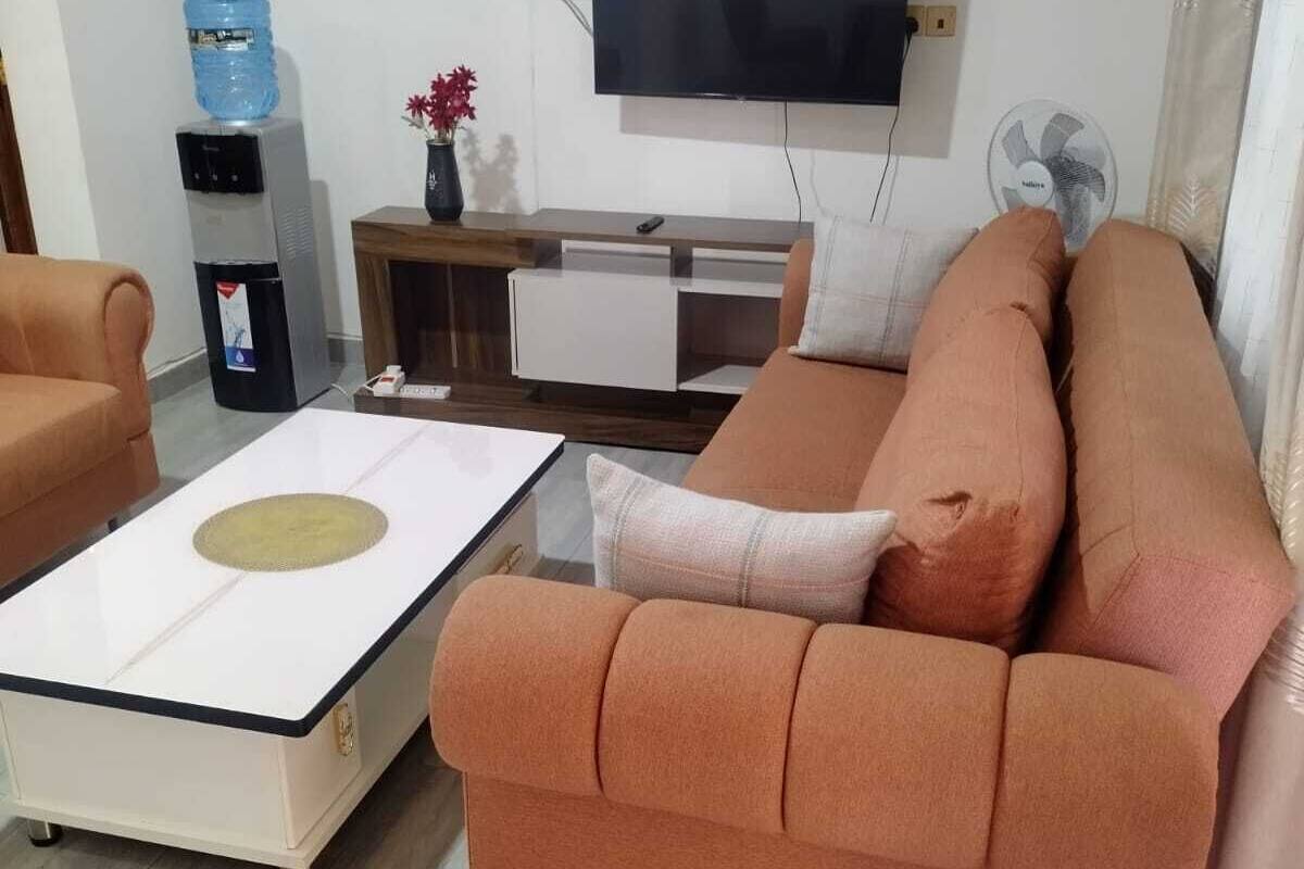 Una sala de estar con sofá, una mesa de centro, dispensador de agua, televisor y un mueble auxiliar.