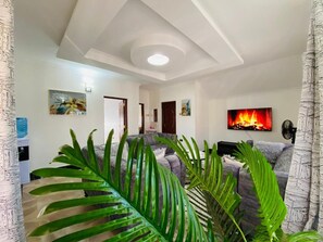 A living room with a grey sofa, a flat-screen TV mounted on the wall, and a fireplace with a visible fire. - Nati Apartments Kisumu (Kisumu)