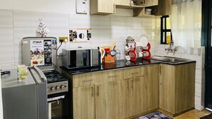 A compact kitchen with a gas stove, a standing mixer, wooden cabinets, and a black countertop. - Nati Apartments Kisumu (Kisumu)