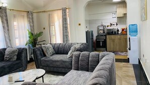 A living room with a sofa set, a coffee table, and a kitchen in the background. - Nati Apartments Kisumu (Kisumu)