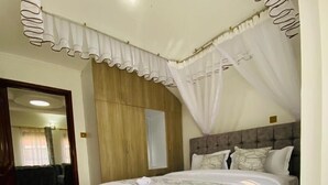 A bedroom with a large bed, a wooden wardrobe, a ceiling fan, and a tiled floor. - Nati Apartments Kisumu (Kisumu)