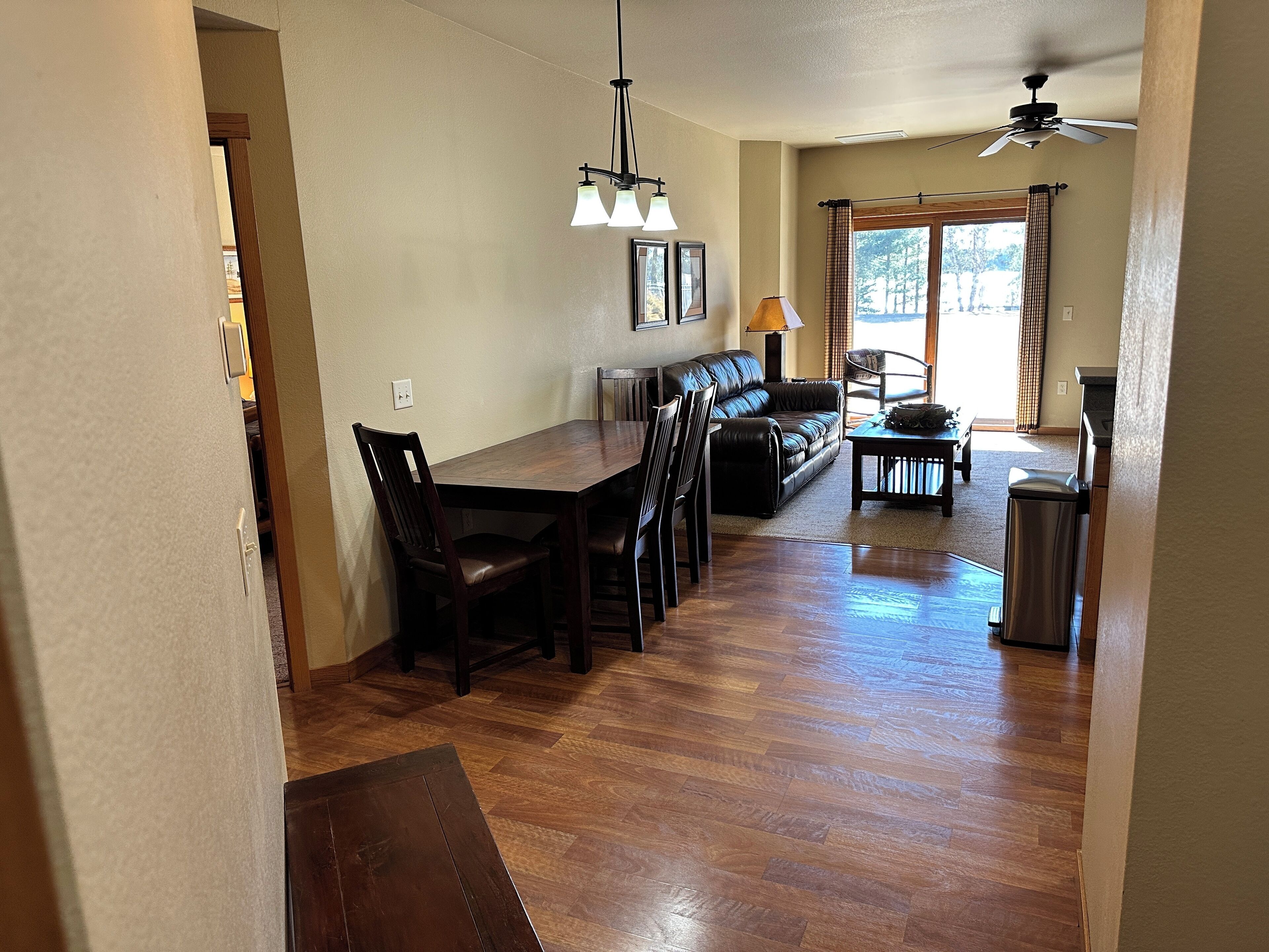 A spacious dining area with a wooden table and chairs, a sofa, and a ceiling fan.