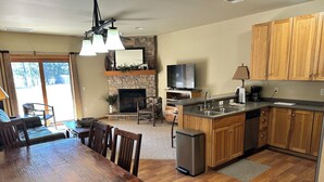 A spacious kitchen with wooden cabinets, a stone fireplace, a dining area with a wooden table and chairs, and a television above the fireplace. - CONDO 106 by Eagle Waters Resort (eagle river)
