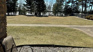 A grassy outdoor area with a paved walkway, surrounded by tall trees and a brick building. - Spirit of the Northwoods (eagle river)