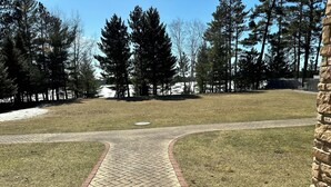 A paved pathway leading to a grassy area with trees and a stone wall. - CONDO 107 by Eagle Waters Resort (eagle river)