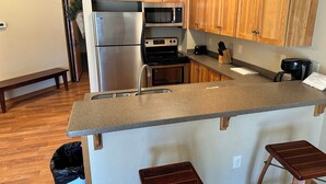 A compact kitchen with wooden cabinets, stainless steel appliances, a granite countertop, and a small bar stool. - Spirit of the Northwoods (eagle river)