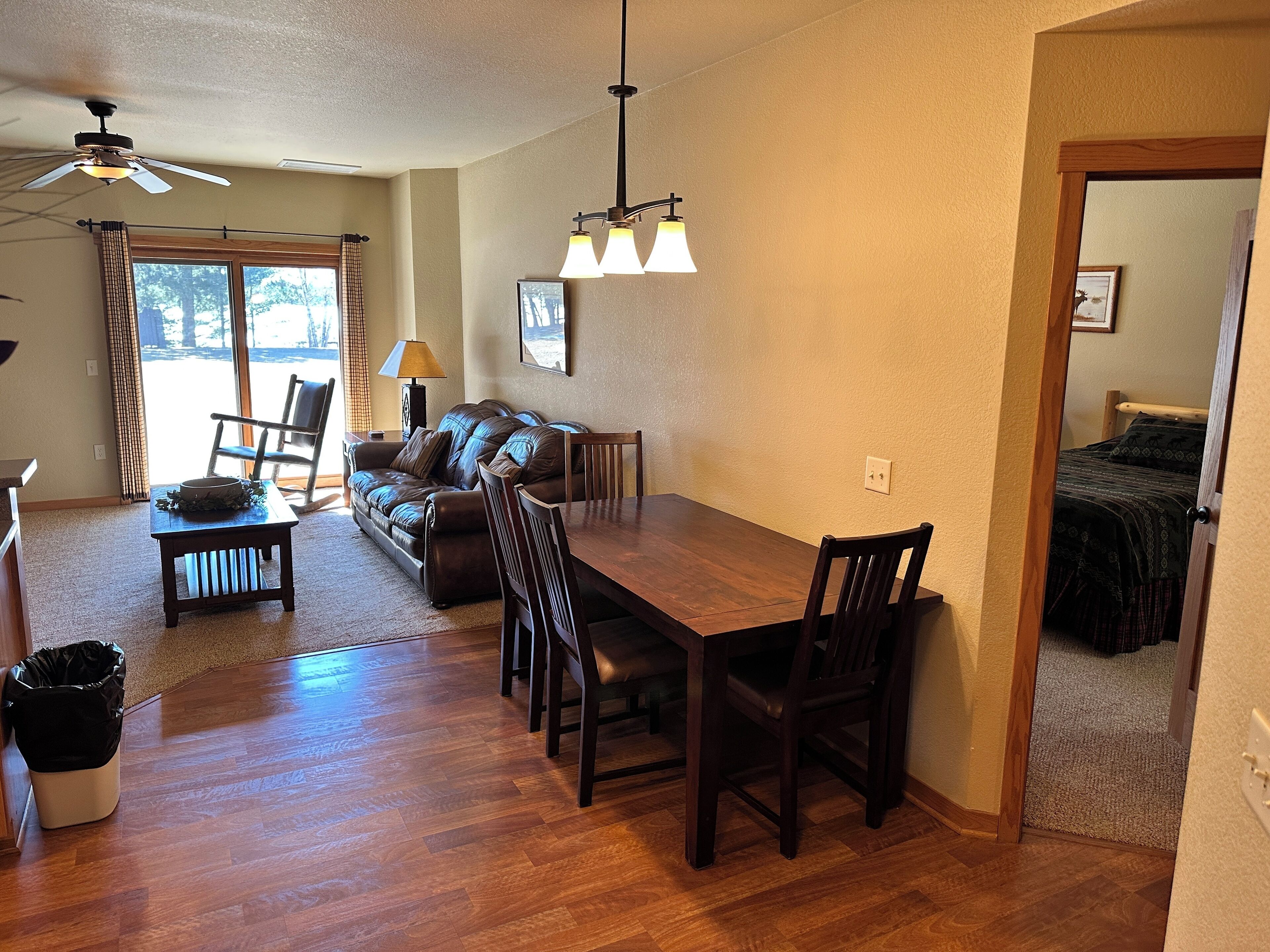 A spacious living room with a wooden dining table, leather sofa, and a ceiling fan.