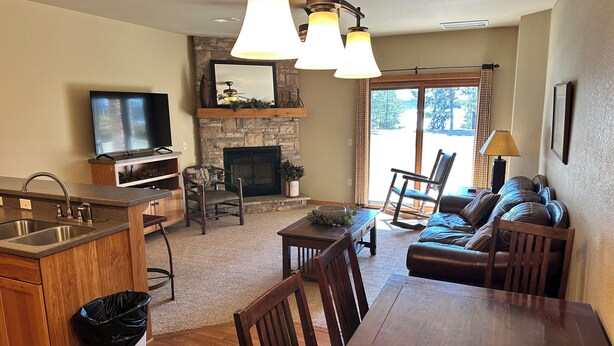 A cozy living room with a fireplace, a dining area, and a kitchen with a built-in TV. - Spirit of the Northwoods (eagle river)
