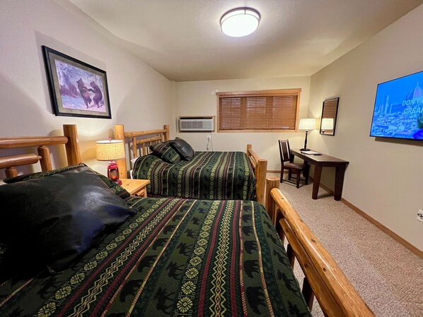 A room with two beds, a desk, a chair, a television, and a framed picture on the wall.
