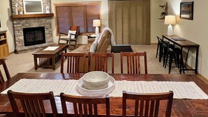 Un comedor con una mesa y sillas de madera, una chimenea, un televisor y un ventanal con persianas.