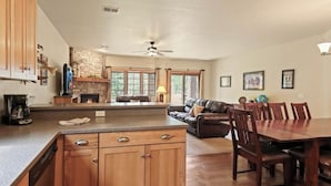 Una cocina amplia con armarios de madera, un comedor con una mesa grande y sillas, una chimenea y una sala de estar con un sofá y televisión.
