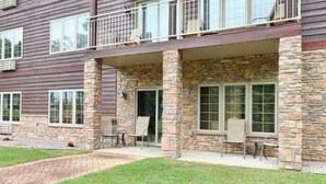 Un edificio de dos pisos con pilares de piedra, ventanas amplias y un patio cubierto con mobiliario exterior.