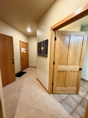 A hallway with carpeted flooring, wooden doors, and a framed picture on the wall.