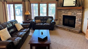 A living room with a stone fireplace, leather sofas, and a wooden coffee table. - Spirit of the Northwoods (eagle river)