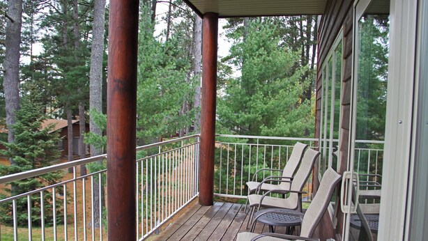 Une terrasse en bois avec des rampes en métal, entourée d’arbres.