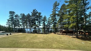 A grassy area with a paved walkway, surrounded by tall trees and a body of water in the background. - CONDO 202 by Eagle Waters Resort (eagle river)