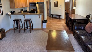 A modern kitchen with wooden cabinets, a stainless steel refrigerator, and a bar area with stools. - CONDO 202 by Eagle Waters Resort (eagle river)