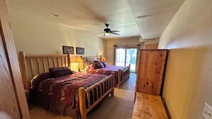 A bedroom with two wooden beds, a ceiling fan, and a view of the outdoors through a sliding glass door. - CONDO 202 by Eagle Waters Resort (eagle river)