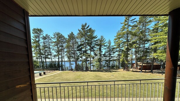 A wooden deck with a metal railing overlooking a grassy area with trees and a lake. - CONDO 202 by Eagle Waters Resort (eagle river)