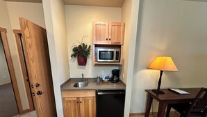 A compact kitchen with a microwave, sink, and dishwasher. There's a small table with a lamp and a chair. - Studio 212 By Eagle Waters Resort (eagle river)