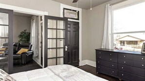 A bedroom with a bed, a dresser, a chair, and a door leading to a balcony.