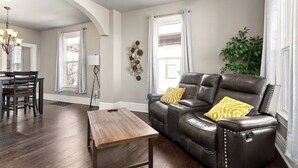 A living room with a dark leather sofa, a wooden coffee table, and a dining area with a table and chairs.