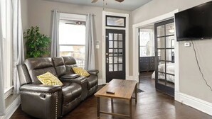 A living room with a leather sofa, a wooden coffee table, a ceiling fan, and a TV mounted on the wall.