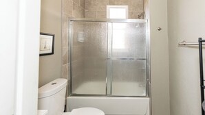 A bathroom with a glass-enclosed shower, a toilet, and a framed picture on the wall.