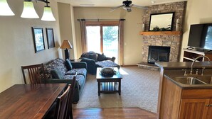 A living room with a fireplace, a dining area with a wooden table and chairs, and a kitchen with a sink and countertop. - Condo 206 W/ Garage by Eagle Waters Resort (eagle river)