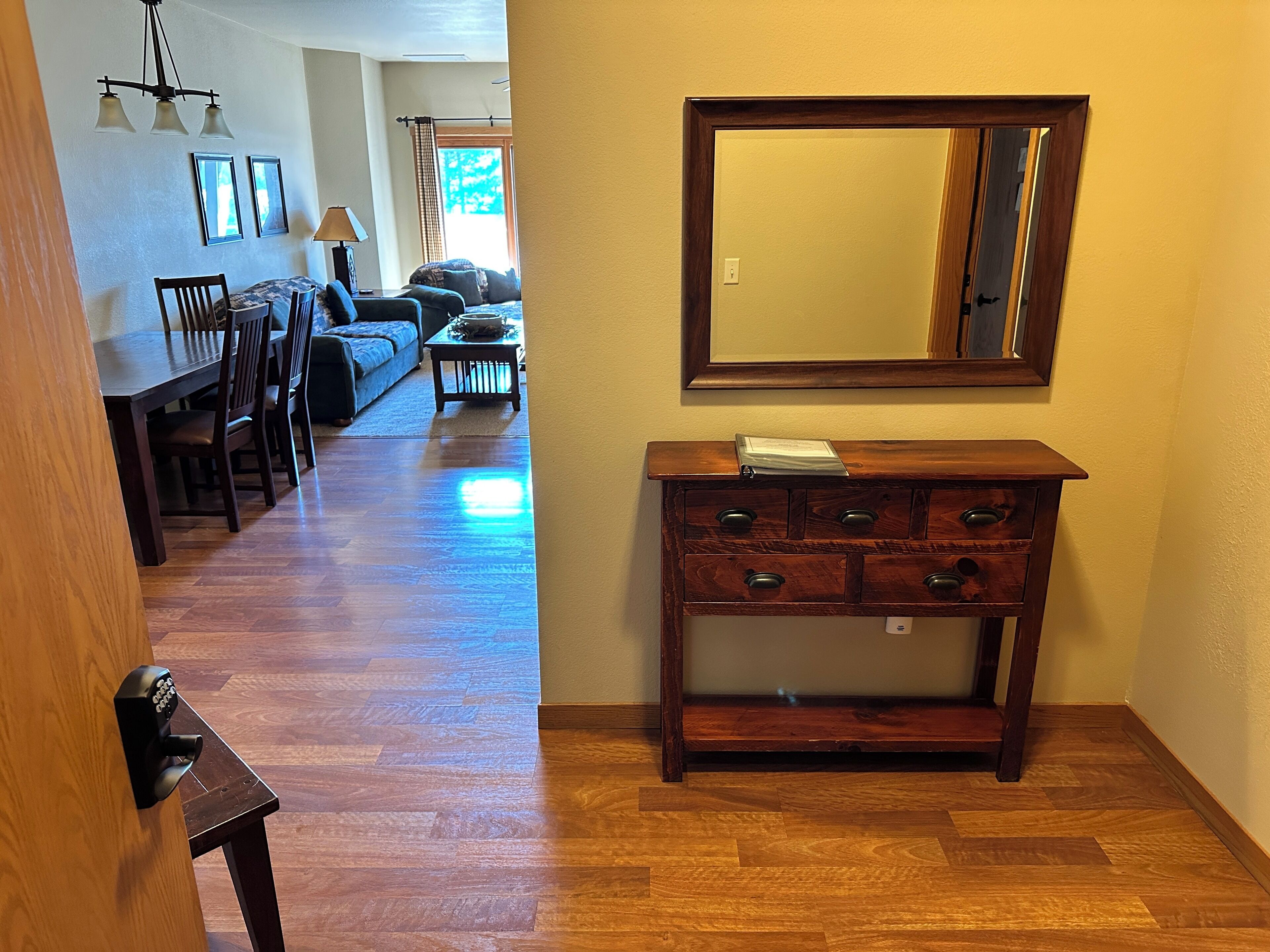 Un couloir avec un plancher en bois, un coin repas avec une table et des chaises, un canapé et un miroir au mur.