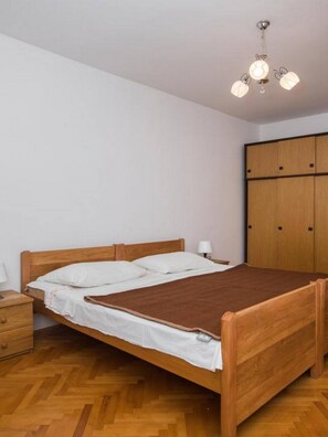 A single bed with a wooden frame, a bedside table, a nightstand, a wardrobe, and a hanging light fixture.