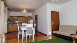 A living room with a sofa, a dining table with chairs, a chandelier, and a kitchen area with wooden cabinets and a refrigerator. - Apartment in Sibenik by Sandy Beaches (Sibenik)