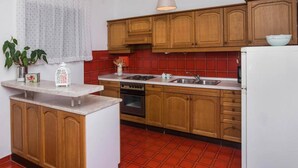 A kitchen with wooden cabinets, a white refrigerator, a red tiled backsplash, and a hanging pendant light. - Apartment in Sibenik by Sandy Beaches (Sibenik)