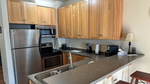 A modern kitchen with wooden cabinets, stainless steel appliances, a granite countertop, and a small wooden stool.