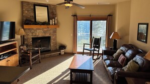 A living room with a stone fireplace, a television, a leather sofa, and a dining table.