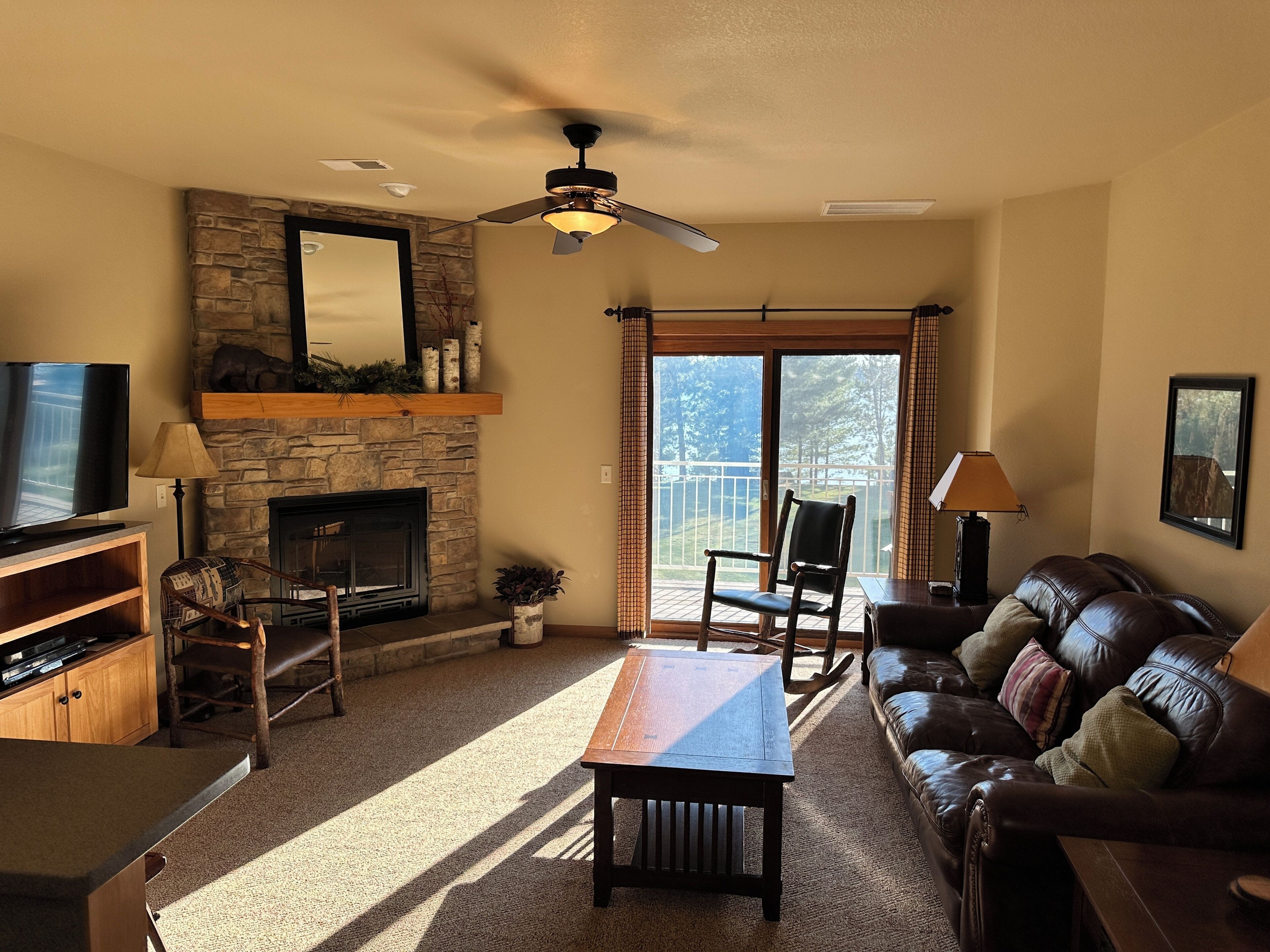 A living room with a stone fireplace, a television, a leather sofa, and a dining table.