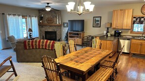A spacious living room with a fireplace, a dining area with wooden furniture, and a kitchen with wooden cabinets. - Spirit of the Northwoods (eagle river)