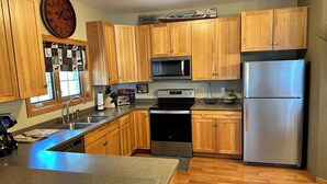 A kitchen with wooden cabinets, a stainless steel refrigerator, a microwave, and a stove. - Spirit of the Northwoods (eagle river)