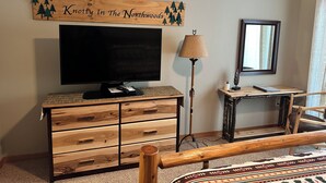 A room with a wooden TV stand, a flat-screen TV, a lamp, a mirror, and a bench. - Studio 311 by Eagle Waters Resort (Eagle river)