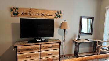 Une pièce comprenant un meuble TV en bois, un téléviseur à écran plat, une lampe, un miroir et un banc.
