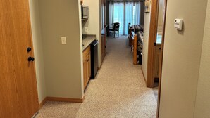 A narrow hallway with a kitchen area on the left, a dining area with a table and chairs in the center, and a bedroom with a bed on the right. - Studio 311 by Eagle Waters Resort (Eagle river)