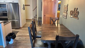 Eine moderne Küche mit Edelstahlgeräten, ein Essbereich mit Holztisch und -stühlen sowie eine Treppe, die zu einer weiteren Ebene führt.