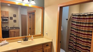A bathroom with a wooden vanity, a large mirror, a toilet, and a striped shower curtain. - Studio 312 by Eagle Waters Resort (eagle river)